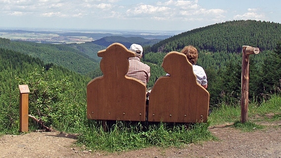 Zwei Menschen sitzen auf einer Bank am Liebesbankweg im Harz und genießen die Aussicht. © Hahnenklee tourismus marketing gmbh 