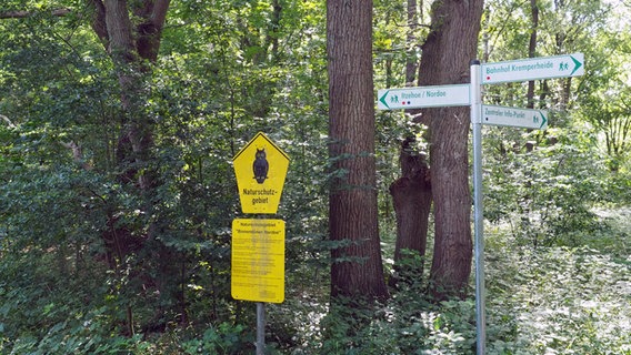 Ein gelbes Schild mit einer Eule und Wegweiser stehen an einem Weg in der Kremperheide. © NDR Foto: Anja Deuble