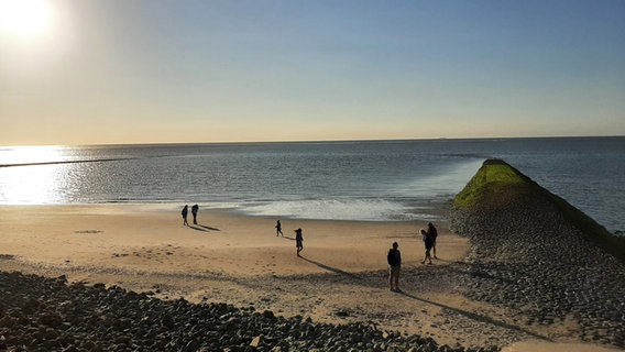 Menschen stehen im Sonnenuntergang am Nordseestrand © NDR Foto: Christina Maciejewski