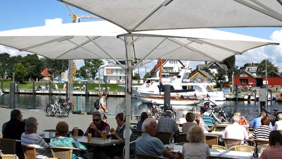 Urlauber sitzen in einem Restaurant im Niendorfer Hafen mit Blick aufs Wasser. © picture alliance/rtn - radio tele nord Foto: Peter Wuest