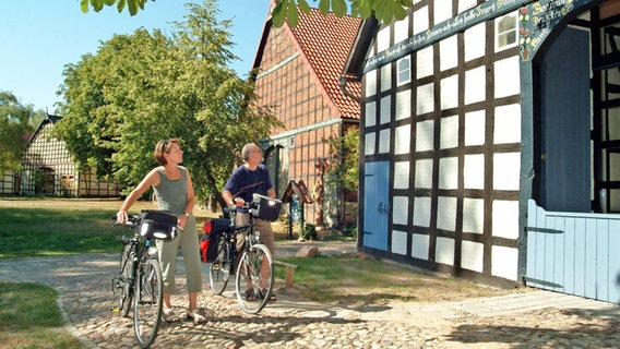 Zwei Radfahrer betrachten ein Haus im Rundlingsdorf Satemin. © dpa - Bildarchiv Foto: Hans-Jürgen Wege