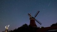 Eine Sternschnuppe leuchtet über den Zwillingsmühlen in Greetsiel in Niedersachsen am Nachthimmel. © picture alliance / dpa Foto: Matthias Balk