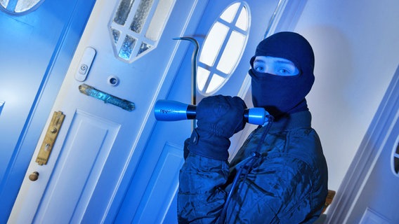 Ein maskierter Mann mit Taschenlampe und Stemmeisen steht vor einer geöffneten Wohnungstür © imago/Schöning 