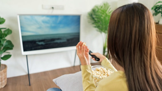 Eine Frau sitzt vor einem Fernseher und hält eine Fernbedienung in der Hand © colourbox 
