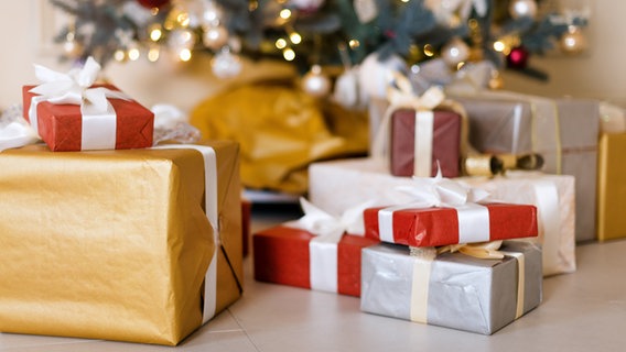Mehrere Weihnachtsgeschenke liegen auf dem Boden, hinten ein Weihnachtsbaum. © Colourbox Foto: levgeniia