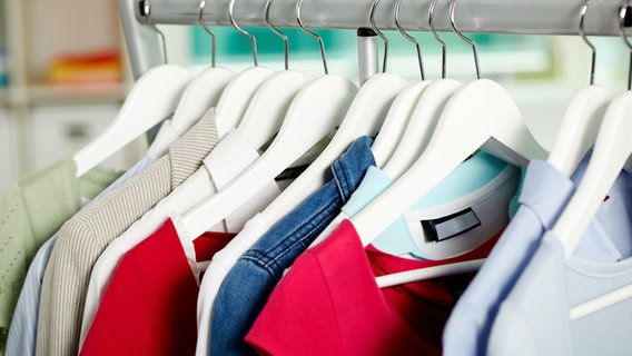 Unterschiedliche Kleidungsstücke hängen auf einer Kleiderstange in einem hellen Raum. © Colourbox Foto: Pressmaster