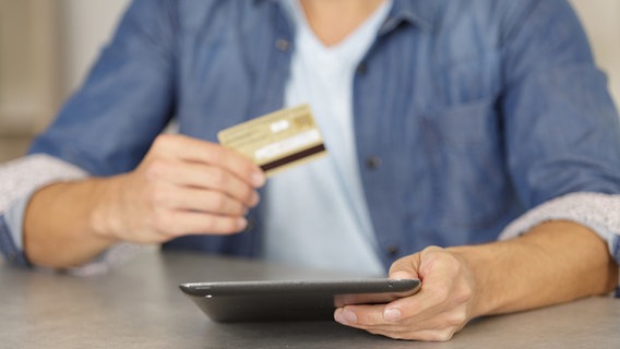 Ein Mann hält ein Tablet und eine Kreditkarte in den Händen. © colourbox 