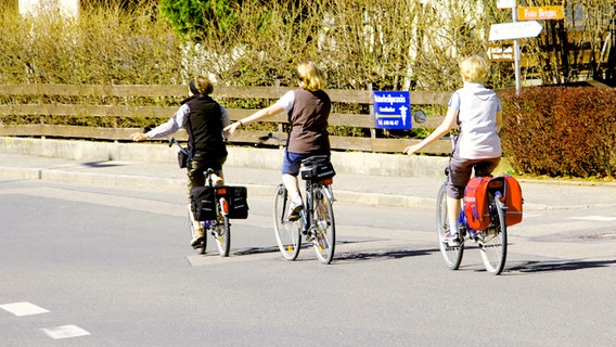 Drei Frauen auf Fahrrädern geben per Handzeichen an, dass sie links abbiegen wollen. © picture-alliance / Paul Mayall 