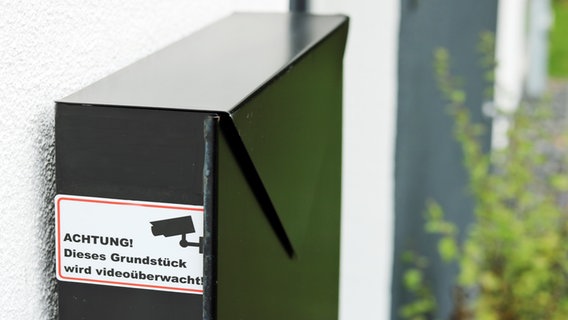 Ein Hinweisschild auf einem schwarzen Briefkasten mit der Aufschrift "Achtung, dieses Grundstück wird videoüberwacht" Ein Hinweisschild auf einem schwarzen Briefkasten mit der Aufschrift "Achtung, dieses Grundstück wird videoüberwacht" © NDR Foto: Elke Janning