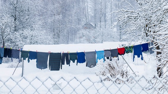Viele Wäschestücke hängen an einer Leine in winterlicher Schneelandschaft © Shutterstock 