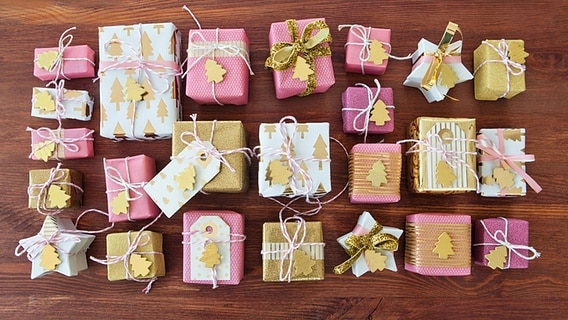 Adventskalender aus kleinen goldenen und rosa Päckchen liegen auf einer Holzplatte. © imago/chromeorange 