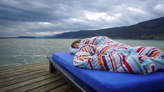 Eine Frau liegt in Decken eingehüllt auf einem Bett auf einem Bootssteg © Photocase Foto: not myself