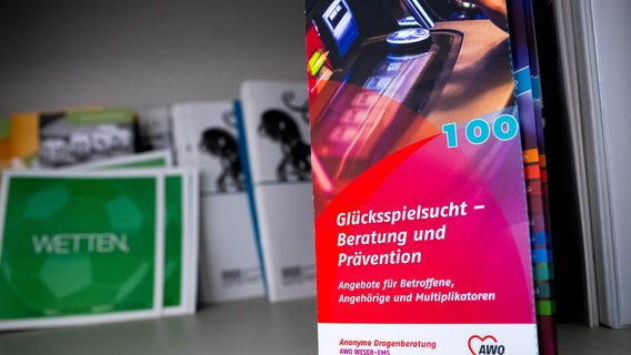 Ein Flyer mit der Aufschrift "Glücksspielsucht - Beratung und Prävention"  liegt 2023 in der Beratungsstelle der anonymen Drogenberatung (drob) in Delmenhorst. © dpa Foto: Sina Schuldt