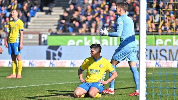 Jannis Nikolaou (M.) von Eintracht Braunschweig sitzt nach seinem Eigentor gegen Hertha BSC frustriert auf dem Rasen © picture alliance/dpa | Swen Pförtner 