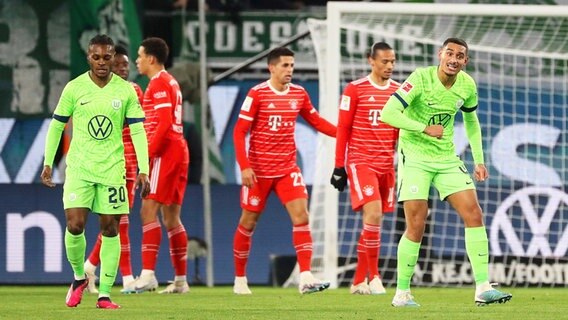 Wolfsburgs Ridle Baku (l.) und Maxence Lacroix sind enttäuscht, während Münchens Spieler im Hintergrund einen Treffer bejubeln. © IMAGO / regios24 