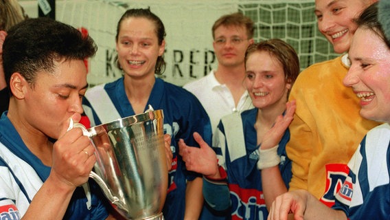 Die Bremerin Michaela Erler (l.) 1995 trinkt aus dem DHB-Pokal Sekt, ihre Mannschaftskollginnen Ignet Ohlmann, Anja Andersen, Klara Orban und Marlies Waelzer (v.l.)  schauen zu. © picture-alliance / dpa Foto: Oliver Berg