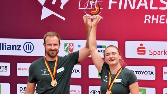 Florian Unruh und Charline Schwarz vom SSC Fockbek halten nach dem Sieg bei den Finals eine Trophäe in die Luft. © Deutscher Schützenbund e.V. Foto: Eckhard Frerichs