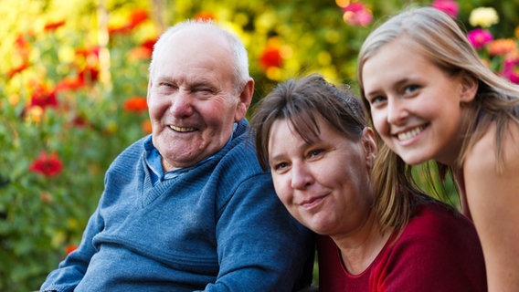 Ein alter Mann, eine Frau mittleren Alters sowie eine junge Frau lächeln in die Kamera. © Colourbox 