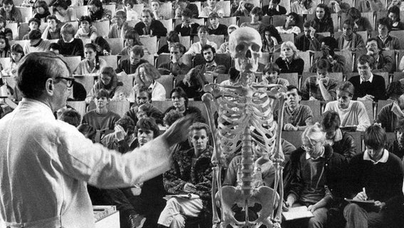 Ein Medizinprofessor steht im Hörsaal vor Studenten und deutet auf ein Skelett. © UKE 