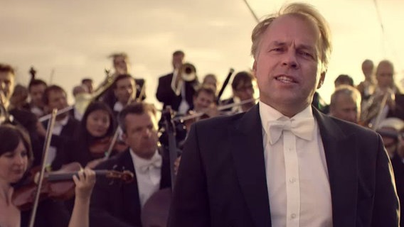 Der Dirigent Thomas Hengelbrock steht vor einem Orchester auf einem Schiff © NDR 