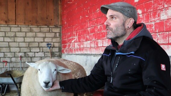 Ein Mann sitzt neben einem Schaf und lächelt in die Kamera. © NDR Foto: Tobias Senff