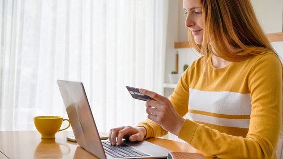 Eine Frau sitzt am Laptop und hat ihre Kreditkarte in der Hand. © imago images 